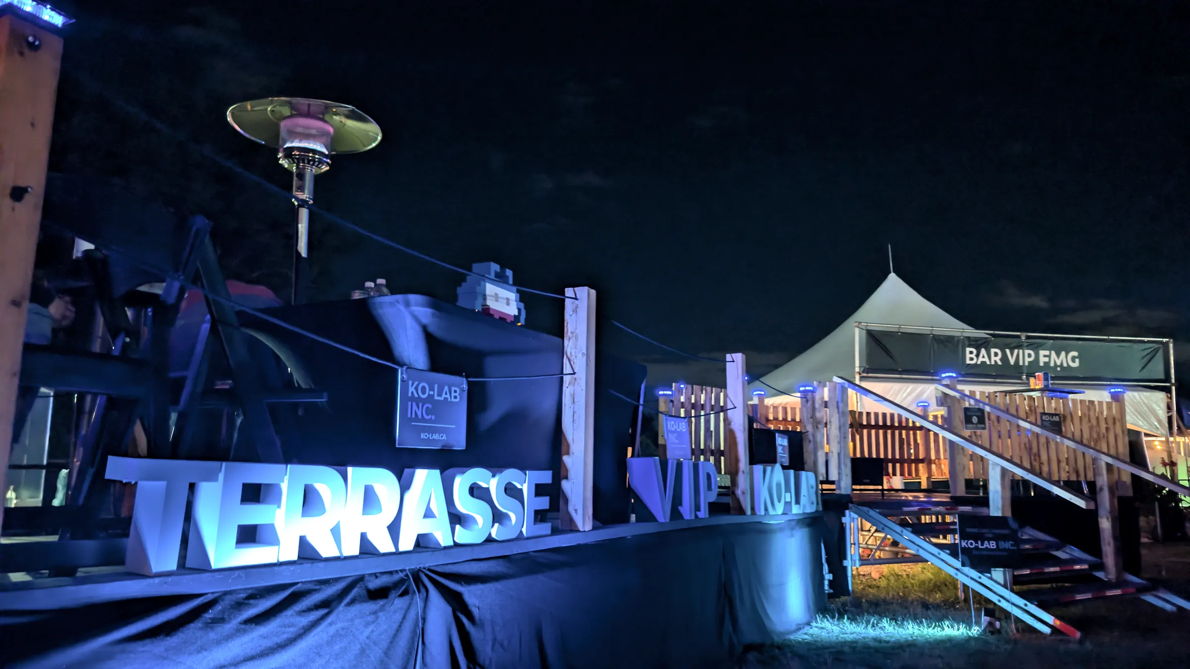 Terrasse VIP KO-LAB illuminée de bleu la nuit, avec bar VIP, sur un site événementiel